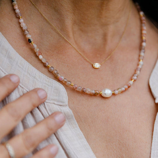 Close-up of a person wearing a delicate Rose Quartz and Pearl necklace with a pearl and gold pendant.