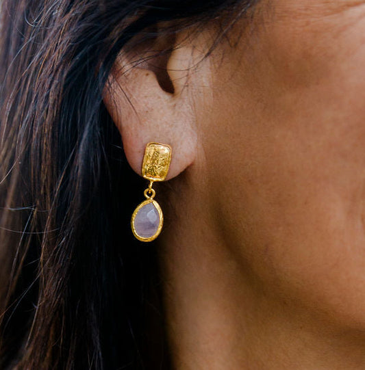 Woman wearing gold moonstone drop earrings with a blurred outdoor background