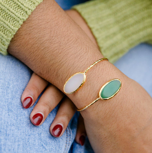 Close-up of a person's wrist wearing two gold bracelets with green and white stones, Two Stone Green Aventurine and Moonstone Bracelet 24k Gold Fill Adjustable Squeeze Cuff