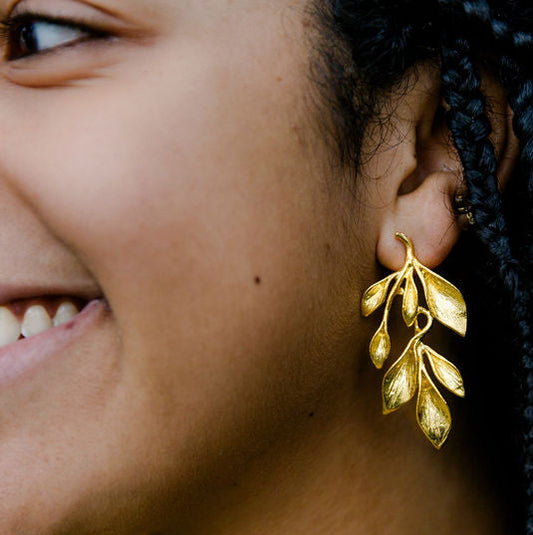Close-up of a woman wearing gold leaf earrings with a blurred green background