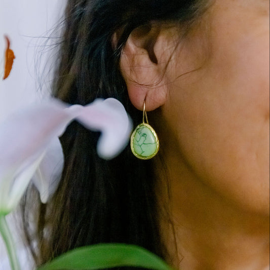 Close-up of a person wearing a gold earring with a turquoise gemstone earrings, holding a white flower.
