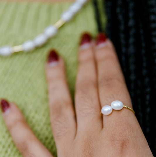 Hand wearing a pearl adjustable ring with a blurred green background