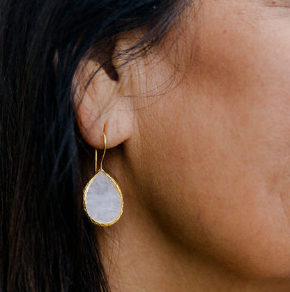 Close-up of a woman wearing a teardrop rose quartz earring with a blurred outdoor background