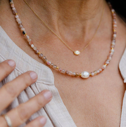 Close-up of a person wearing a delicate Rose Quartz and Pearl necklace with a pearl and gold pendant.