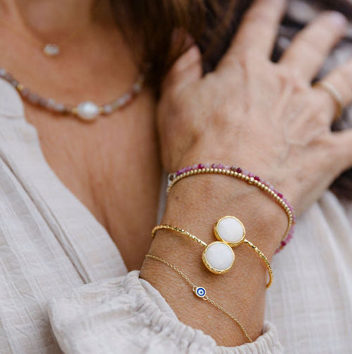 Woman wearing multiple 2 stone mother of pearl adjustable bracelet and a necklace with a blurred background