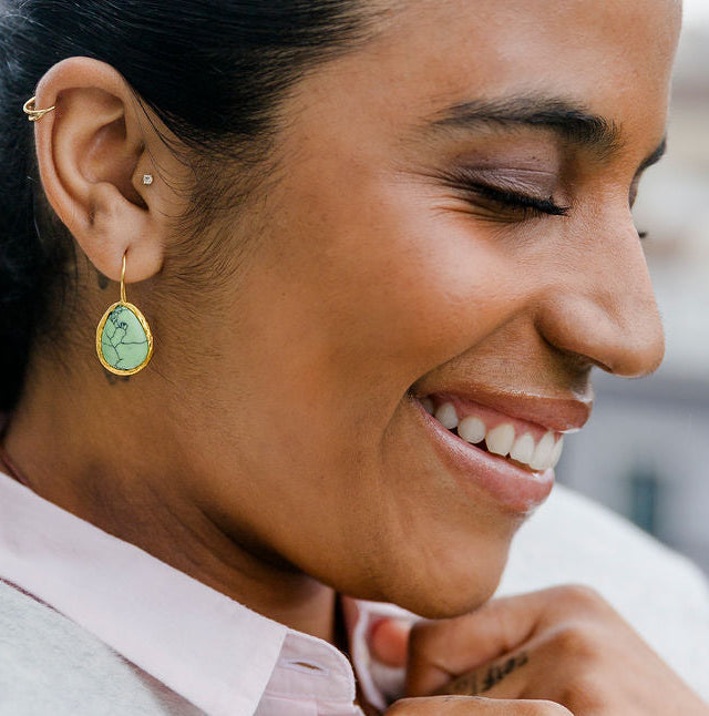 Woman wearing a light gray coat and pink shirt, smiling outdoors.