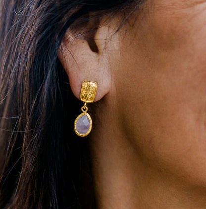 Woman wearing gold moonstone drop earrings with a blurred outdoor background