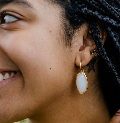 Woman with braided hair wearing a green sweater and gold moonstone drop earring.