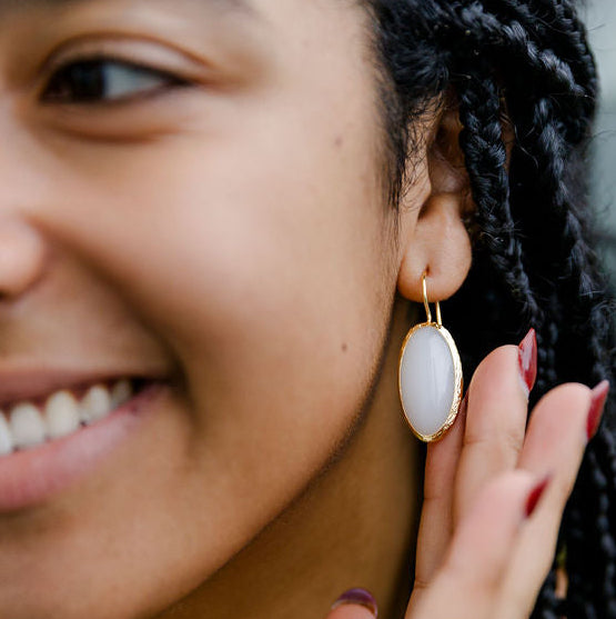 Close-up of a woman wearing gold moonstone drop earrings with a blurred background