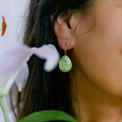 Close-up of a person wearing a gold earring with a turquoise gemstone earrings, holding a white flower.