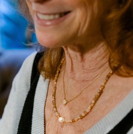 Woman wearing a light gray sweater with black trim, smiling.