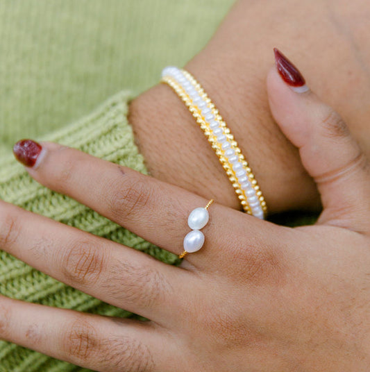 Close-up of hands wearing pearl ring and beaded pearl cuff bracelet on a green background