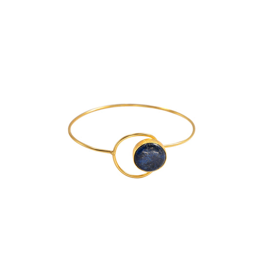 A gold bangle bracelet featuring a central circular gold ring and a dark blue, textured stone inlay, shown against a plain white background.