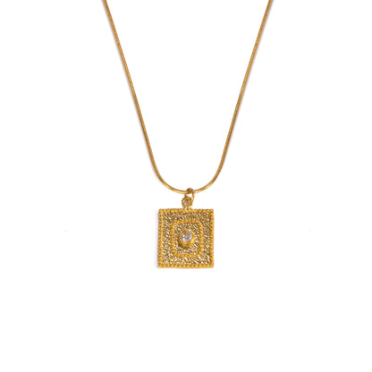 A gold square pendant necklace featuring a textured border and a central clear gemstone, suspended from a delicate gold chain against a plain white background.