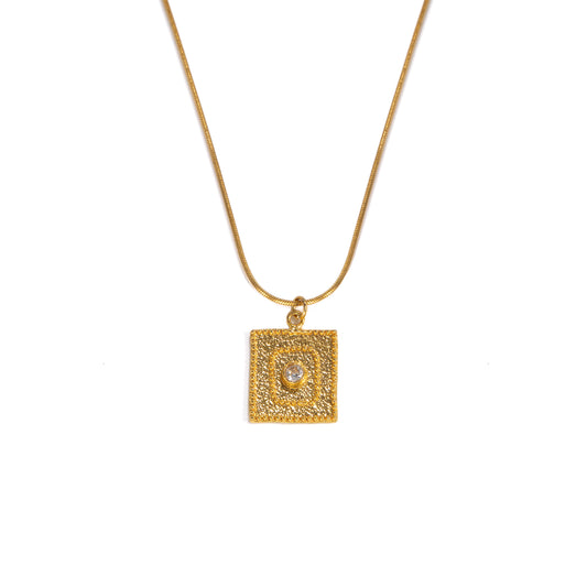 A gold square pendant necklace featuring a textured border and a central clear gemstone, suspended from a delicate gold chain against a plain white background.