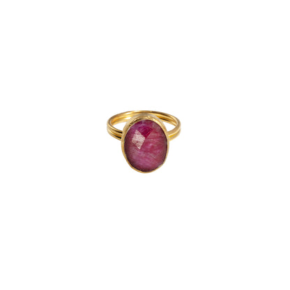 A gold ring featuring an oval-cut pinkish-red gemstone, set against a plain white background.